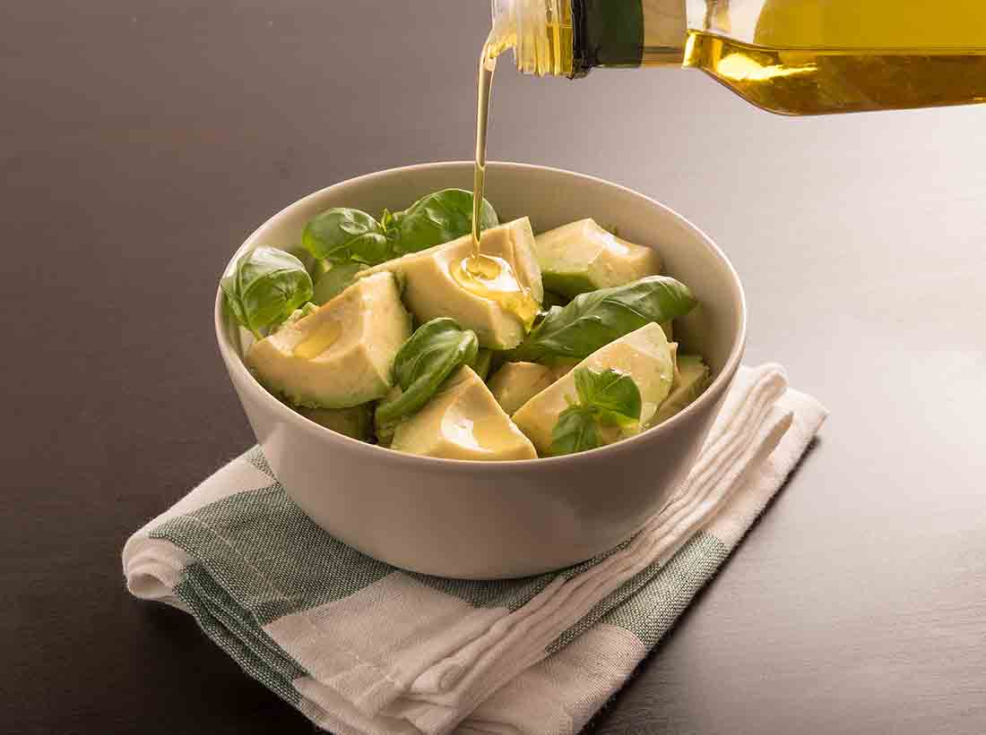 Bottle of Olive Oil Pouring Into Avocado In a Bowl.