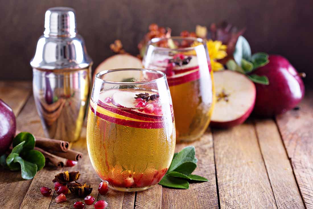 Two Glasses of Cider Next To Apples on a Wooden Surface.