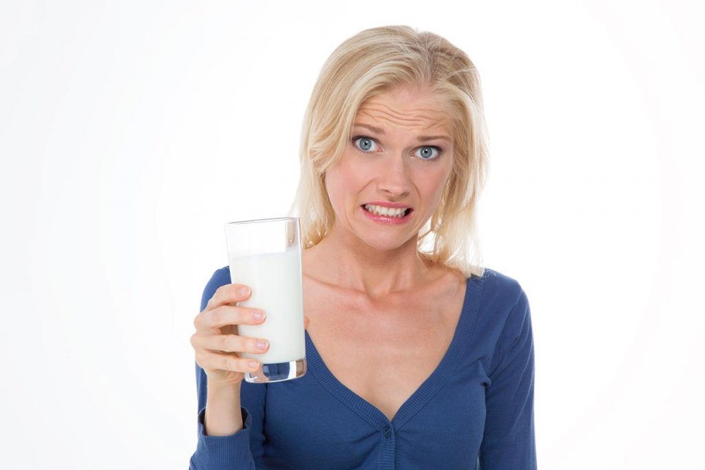 A Woman Holding a Glass of Milk In Her Hands Looking Unsure (lactose intolerance theme).