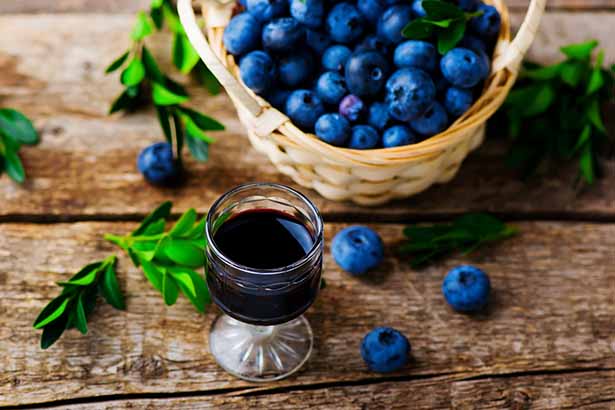 A Glass of Blueberry Wine Next To a Basket of Blueberries.