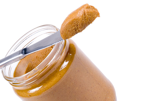 A Glass Jar of Peanut Butter With a Knife Taking Some Out.