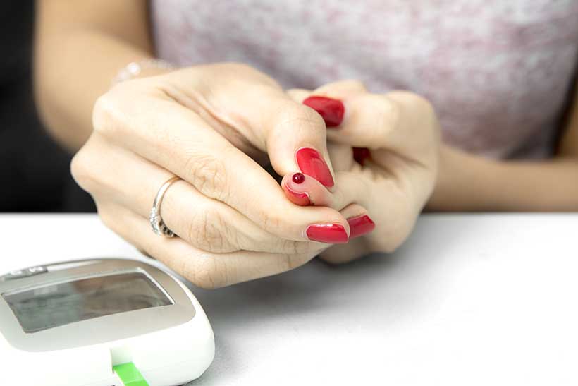 Picture of a Lady Next To a Ketone Blood Meter With Blood on Her Finger.