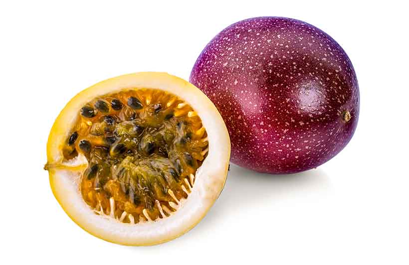 A whole passion fruit next to half a passion fruit showing its inner orange flesh.