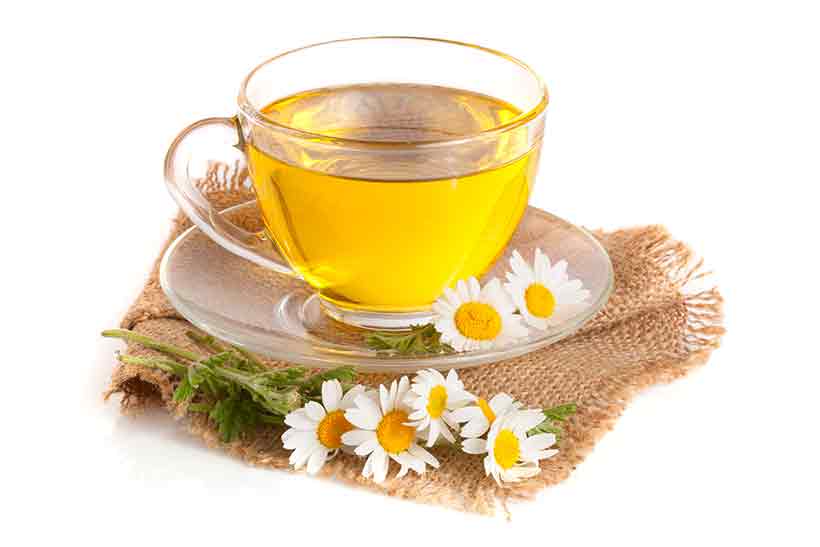 Cup of Chamomile Tea Surrounded by Leaves and Flowers.