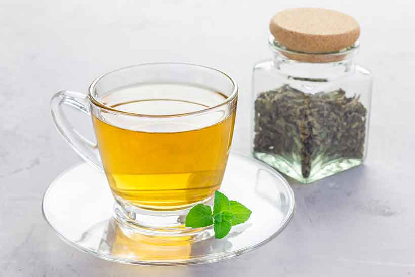 Glass Cup of Peppermint Tea Next To Dried Peppermint Leaves.