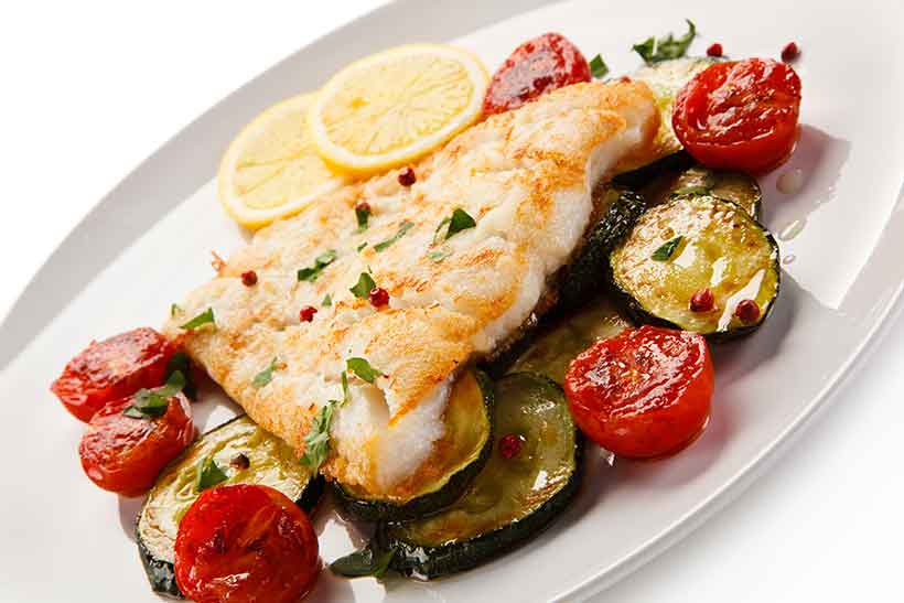 A Roasted Cod Fillet On a Plate With Zucchini Slices and Cherry Tomatoes.