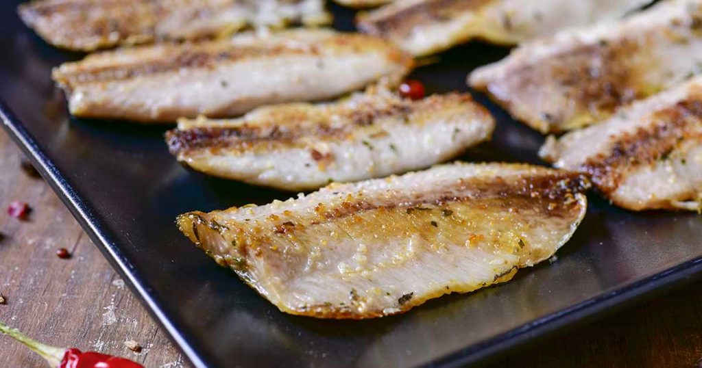 Several grilled sardines next to each other on a black surface.