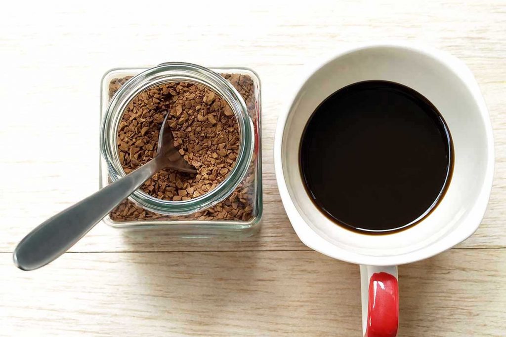A Cup of Instant Coffee Next To An Instant Coffee Jar.