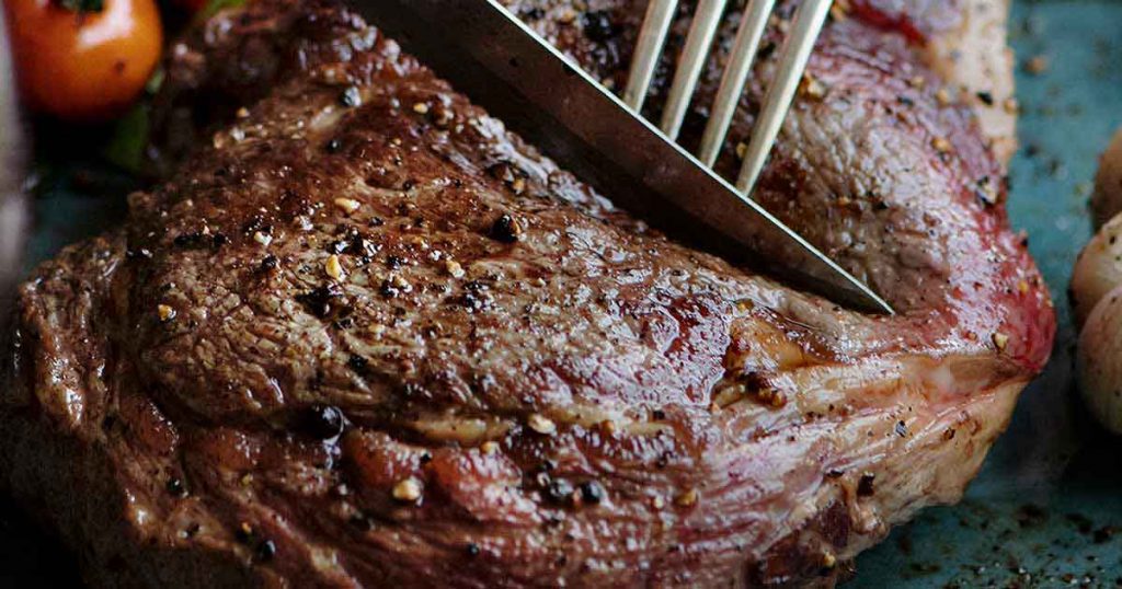 A knife and fork cutting a cooked lamb steak.