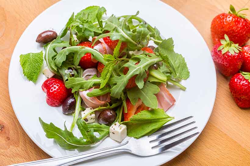 A Greek Salad Featuring Ham, Strawberries, Feta, Salad and Kalamata Olives.