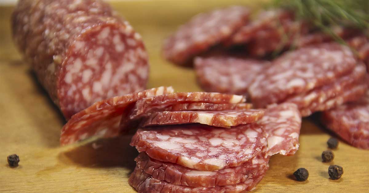 Slices of Salami and a Salami Sausage On a Wooden Board.