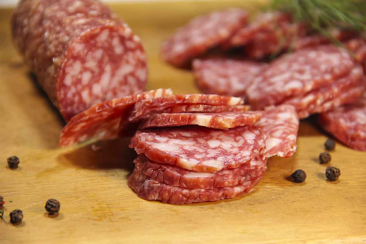 Slices of Salami and a Salami Sausage On a Wooden Board.