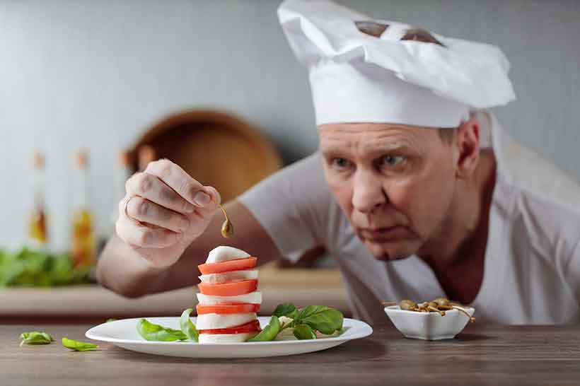 A Chef Decorating a Salad With Capers and Mozzarella.