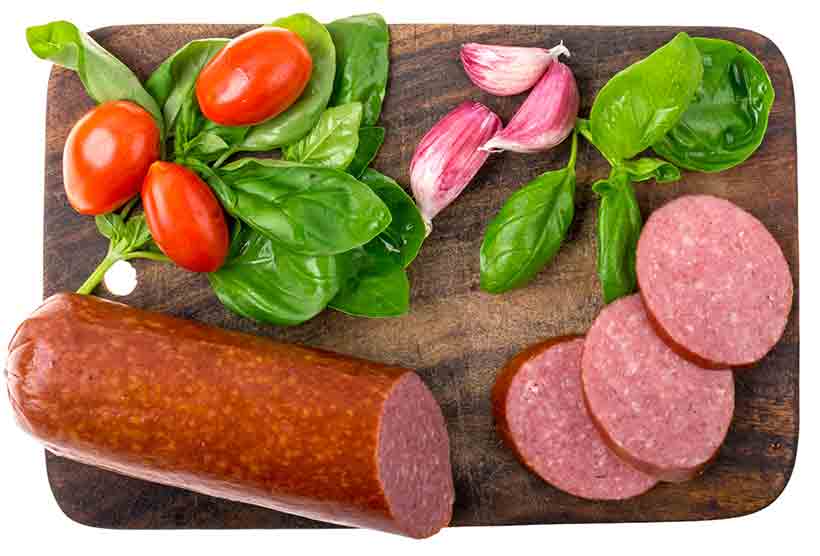 A Salami Sausage, Slices of Salami and Vegetables On a Wooden Board.