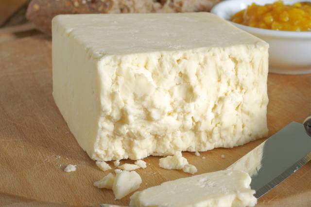 Block of Cheshire cheese on a wooden surface.