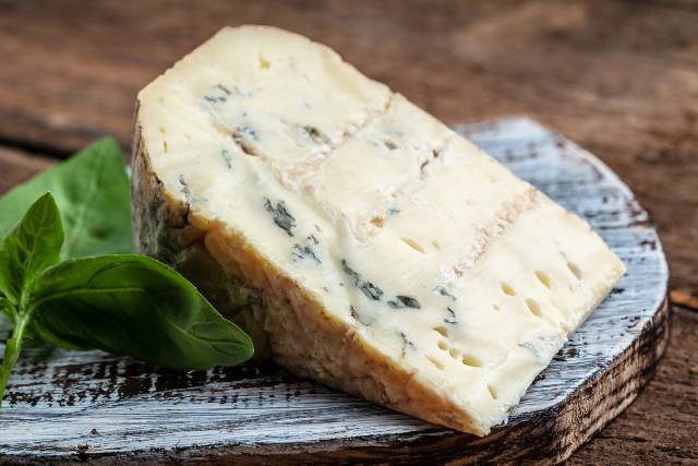 A wedge of Danish Blue cheese on a wooden surface.