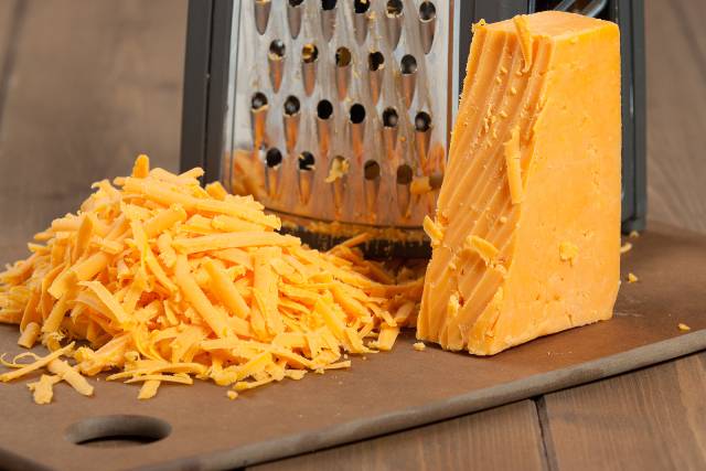 Block of Red Leicester cheese next to a grater with grated cheese in a pile.