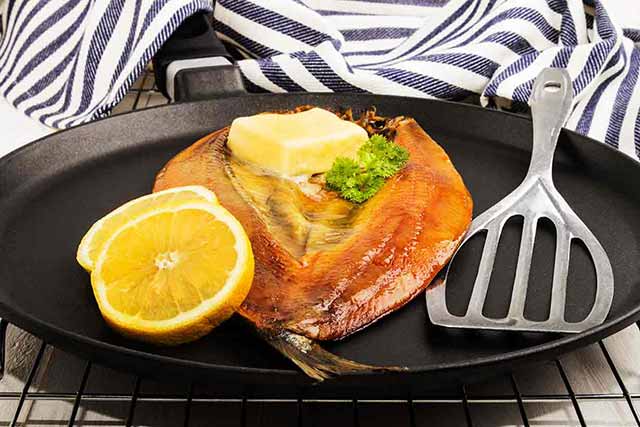 A Kipper In a Cast Iron Skillet With Butter and Lemon Slice.