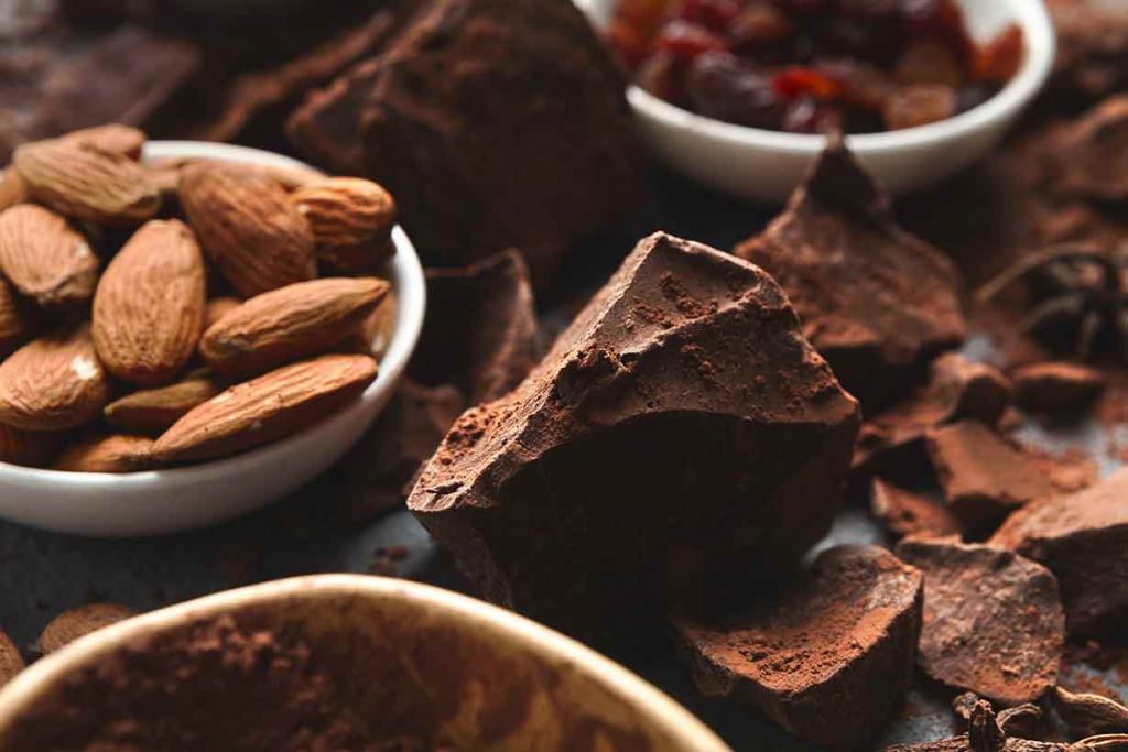 Chunks of Dark Chocolate Surrounded By Cocoa and Cocoa Beans.