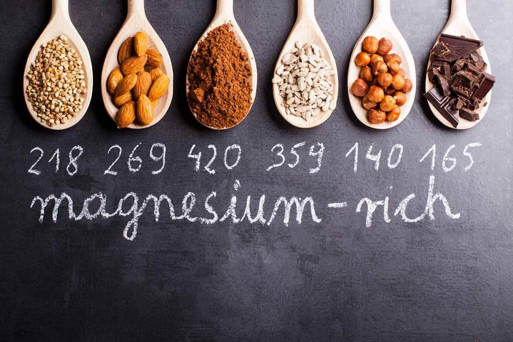 Various foods high in magnesium on wooden spoons - oats, cocoa, almonds, etc.