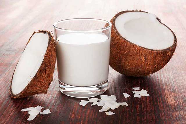 A Glass of Coconut Cream Next To Two Halves of Coconut.