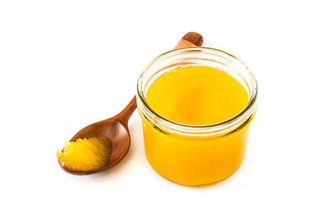Bright Yellow Ghee In a Glass Jar With Wooden Spoon.