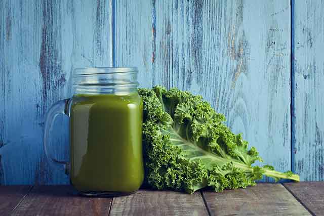 Kale Smoothie In a Glass Jar Next To Fresh Leaves.