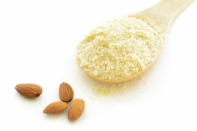 Almond Flour (Almond Meal) On a Wooden Spoon Next To Almonds.