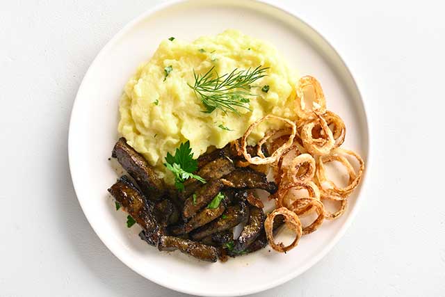 Fried Beef Liver, Onions, and Mashed Potato On a White Plate.