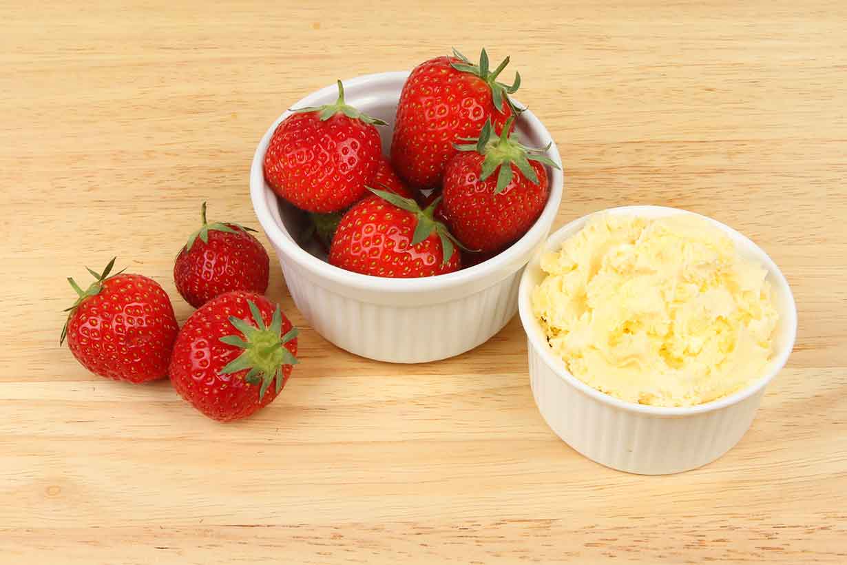 Bowl of Golden Yellow Clotted Cream Next To Bowl of Strawberries.