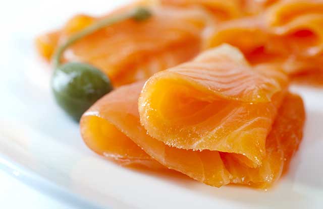 Cold-smoked Salmon Slices On a White Plate Next To Caper Berry.