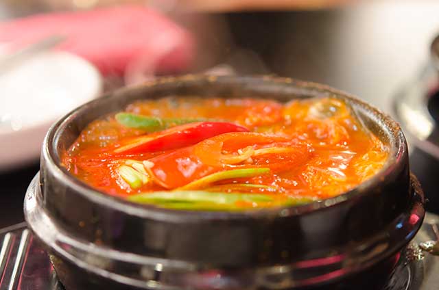 Kimchi Jjigae (Kimchi Stew) In a Black Ceramic Bowl.