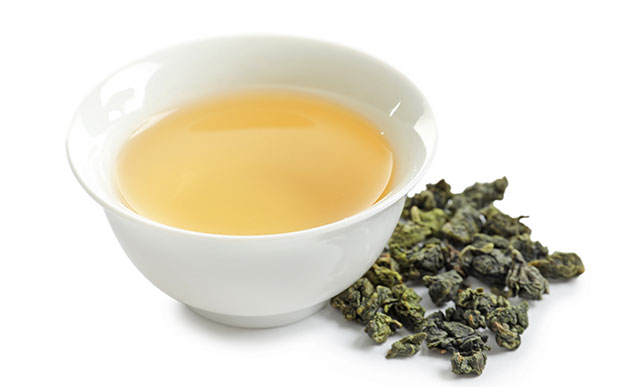 Oolong Tea In a White Cup Next To Tea Leaves,