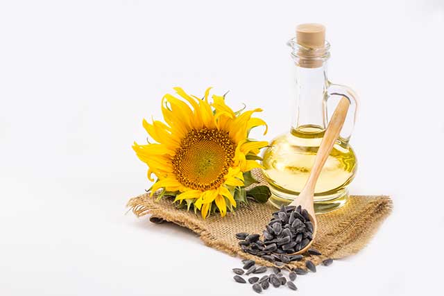 Glass Bottle of Sunflower Oil Next To Flower and Seeds.