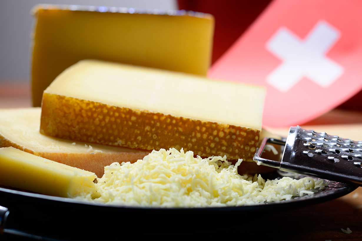 Block of Gruyere Cheese and Shredded Cheese On a Black Plate.