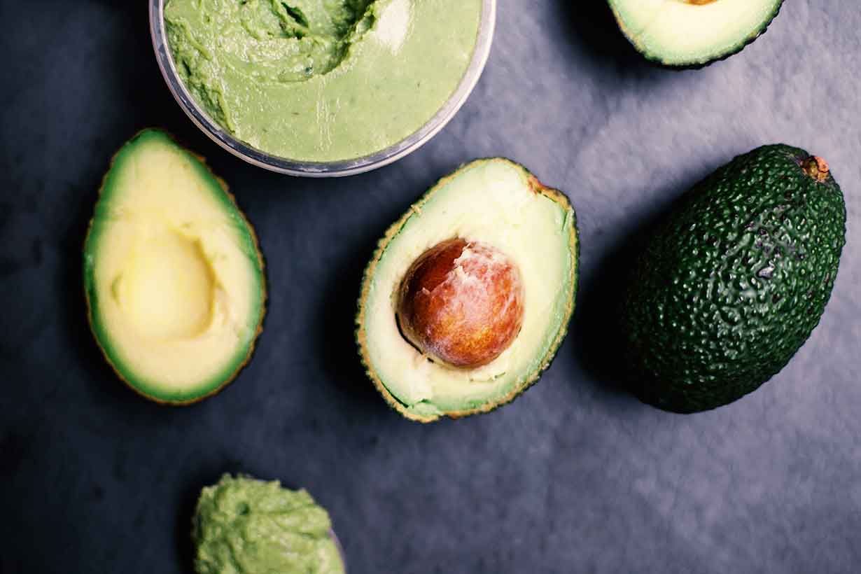 Avocados Sliced In Half Next To Bowl of Guacamole.