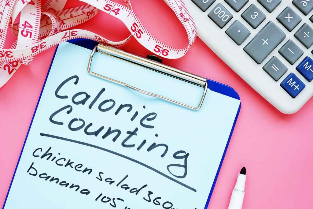 Notepad Saying "Calorie Counting" On a Pink Table.