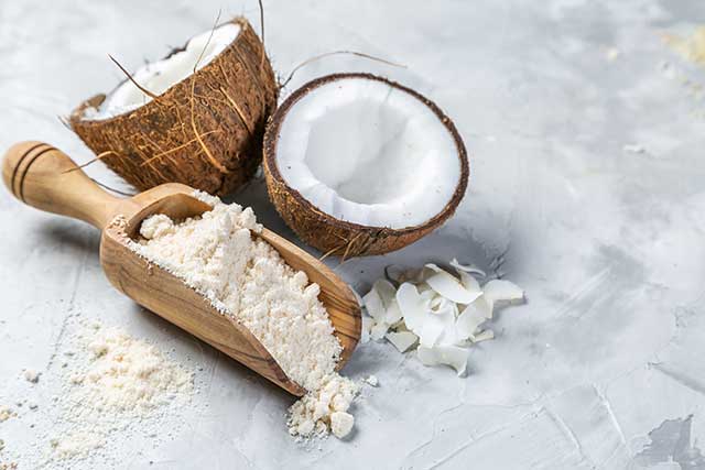 Coconut Flour Next To Two Coconut Halves.