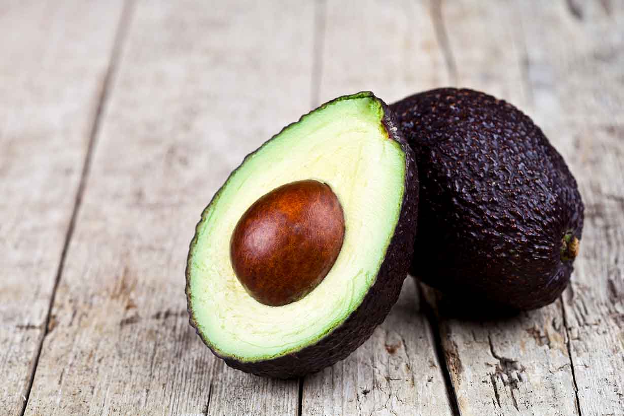 Whole and Half Avocado On a Wooden Surface.