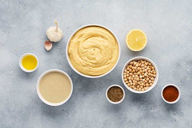 A Bowl of Hummus Next To the Ingredients Used To Make It.