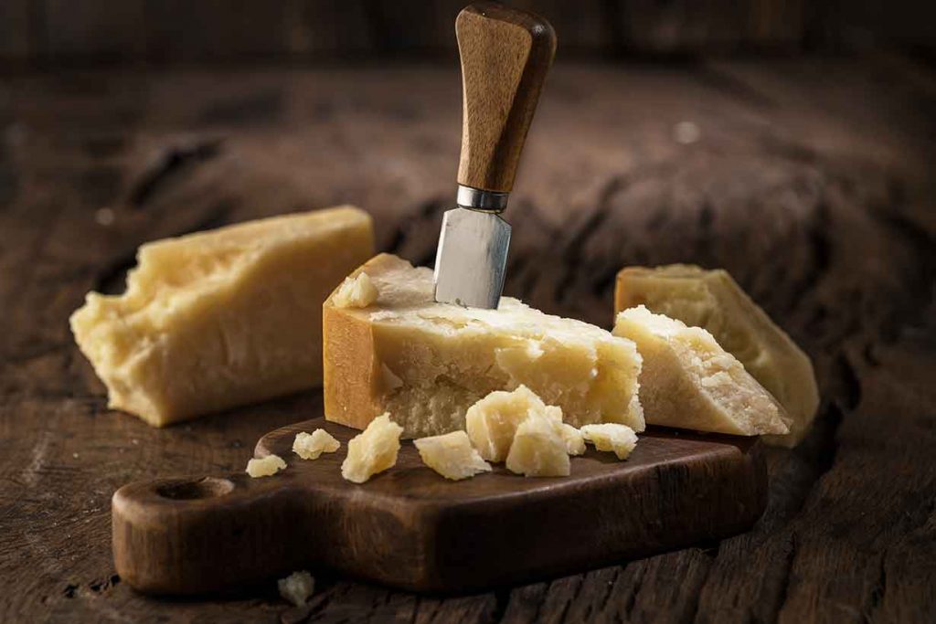 Hard and crumbly aged cheese on a wooden board.
