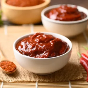 Gochujang in a white bowl next to chili peppers.