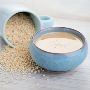 Tahini in a blue bowl next to sesame seeds.