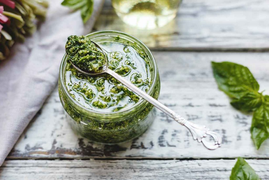 A Spoon On Top of a Glass Jar of Basil Pesto.