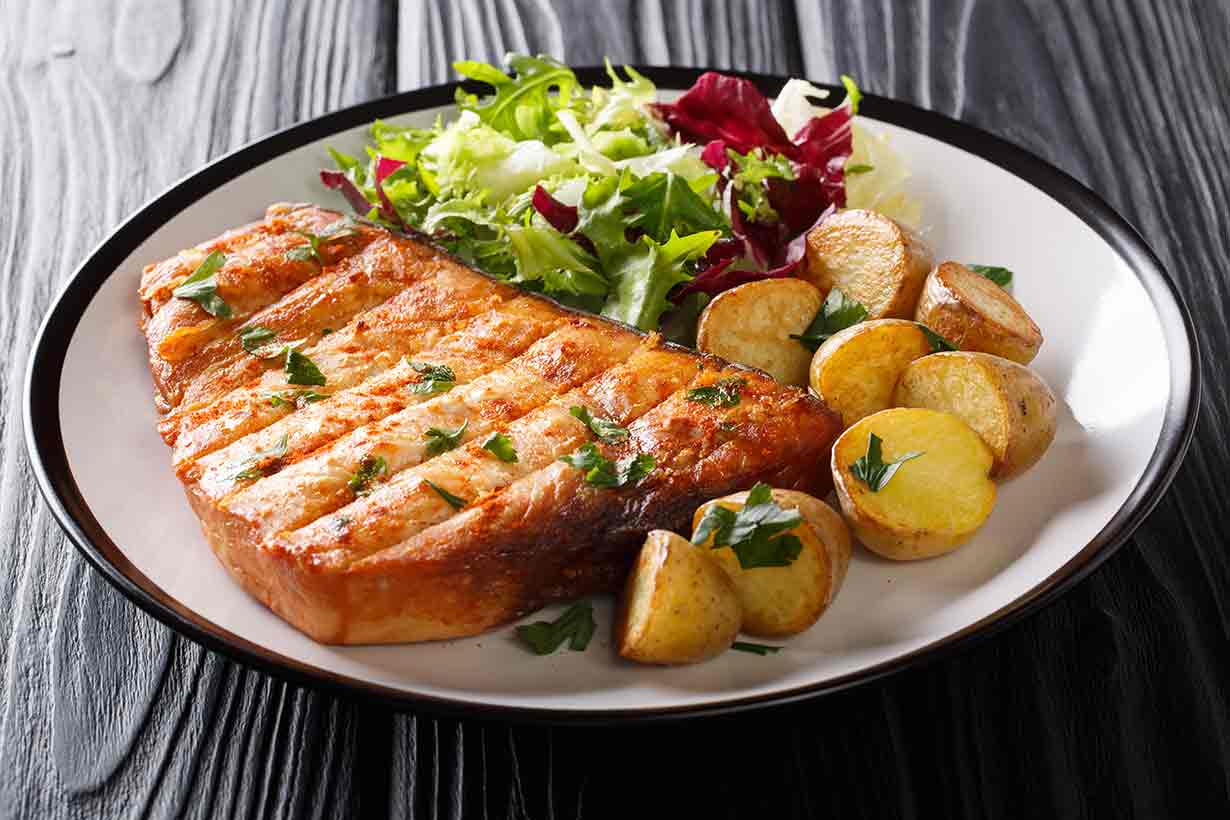 A Thick Cut of Swordfish Served With Salad and Potatoes.