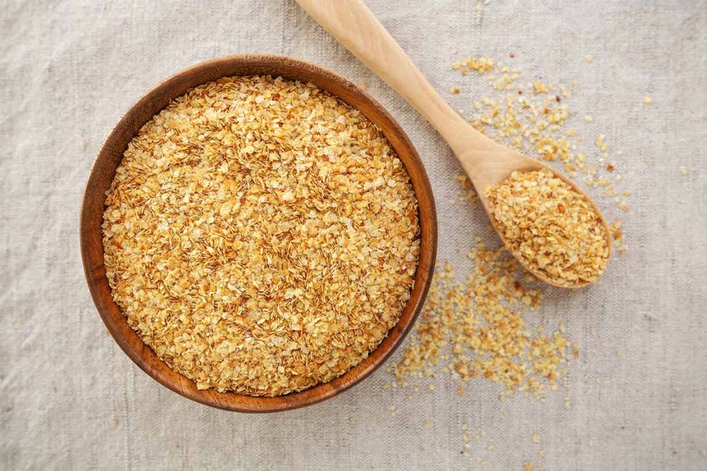 A Bowl of Wheat Germ Next To a Wooden Spoon.