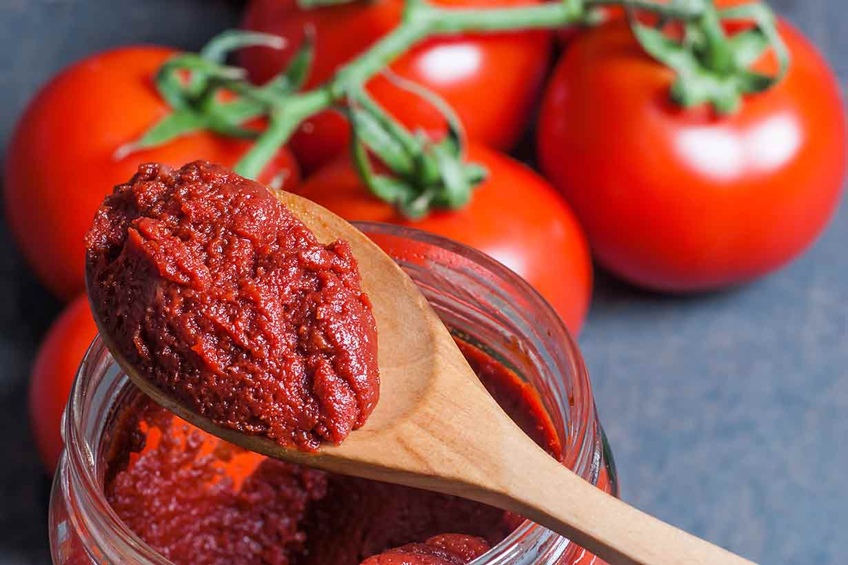 Tomato Paste On a Wooden Spoon With Whole Tomatoes in the Background.