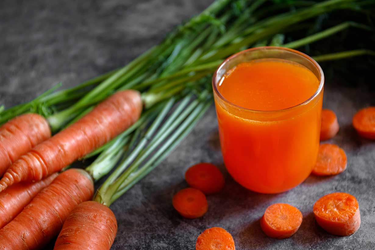 A Glass of Orange Juice Next To Whole Carrots.