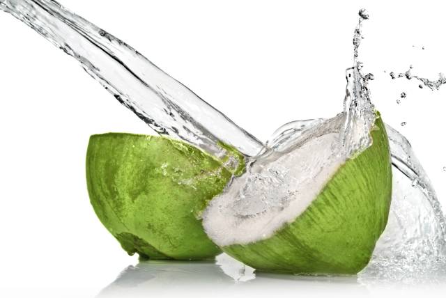 Fresh green coconut cut in half with coconut water spilling out of it.