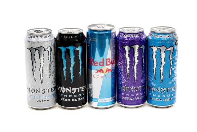 Various cans of energy drinks in a line (Red Bull, Monster).